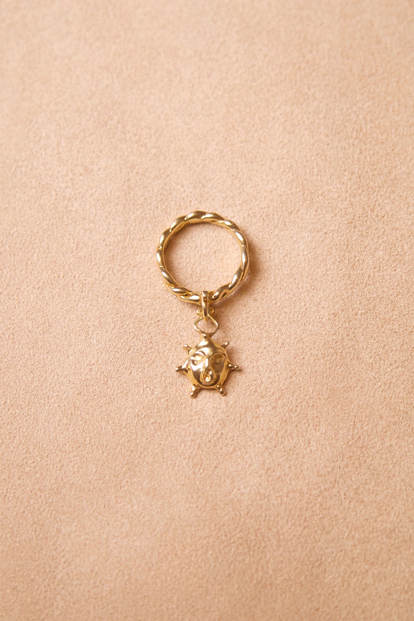 CLARK Aurora Charm ring rests on pink suede. The ring features a twisted 18K Gold Vermeil band with a sun face charm. This is a unique statement ring made using the lost wax casting method. A radiant gift for someone who likes renaissance inspired jewelry.