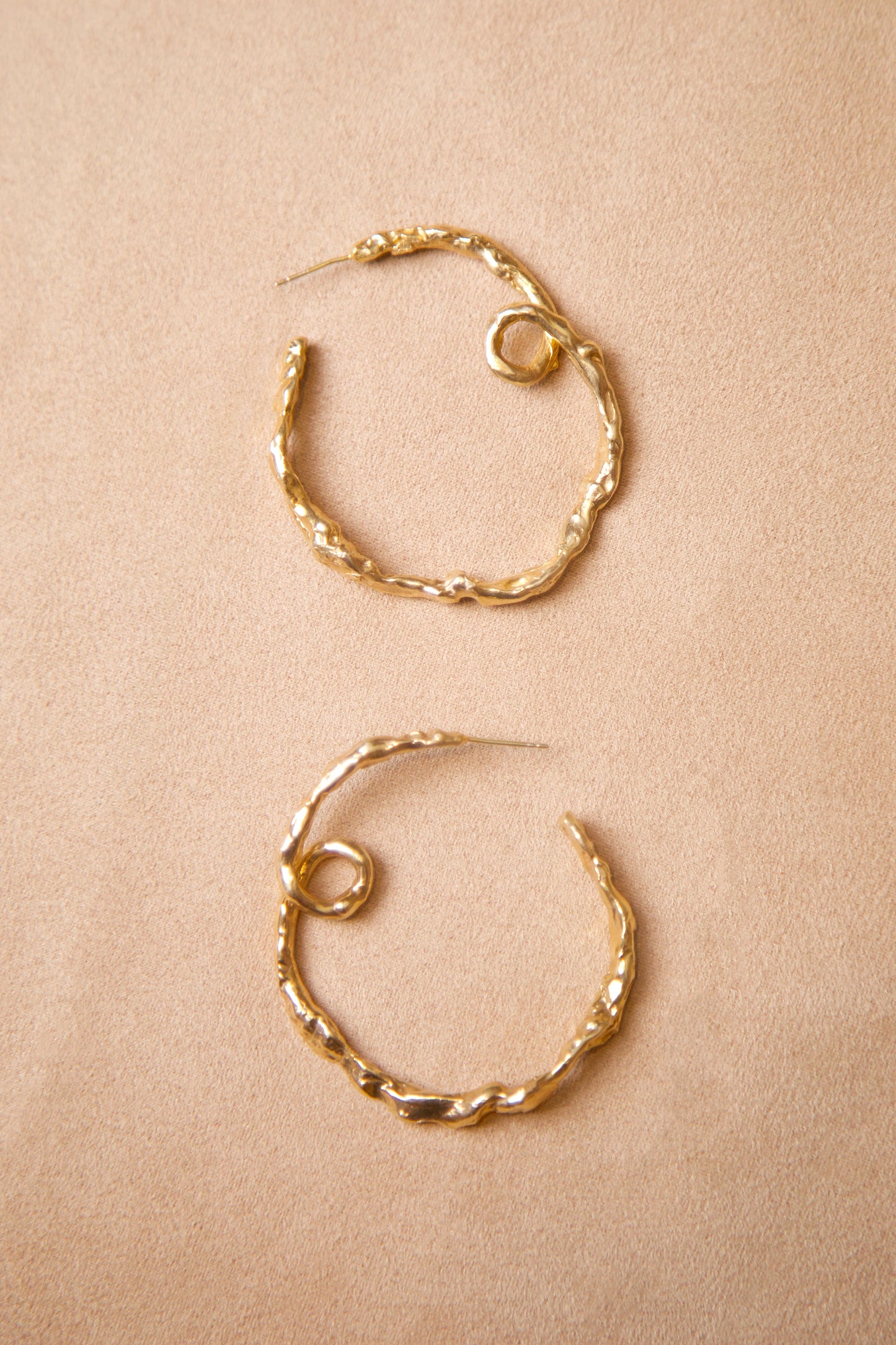 18K Gold Vermeil CLARK Medusa Curl Hoop earrings delicately laid side by side on suede. The unique design is hand made using the lost wax casting method. These sculptural hoops reference a ringlet of hair from the Greek Medusa myth.