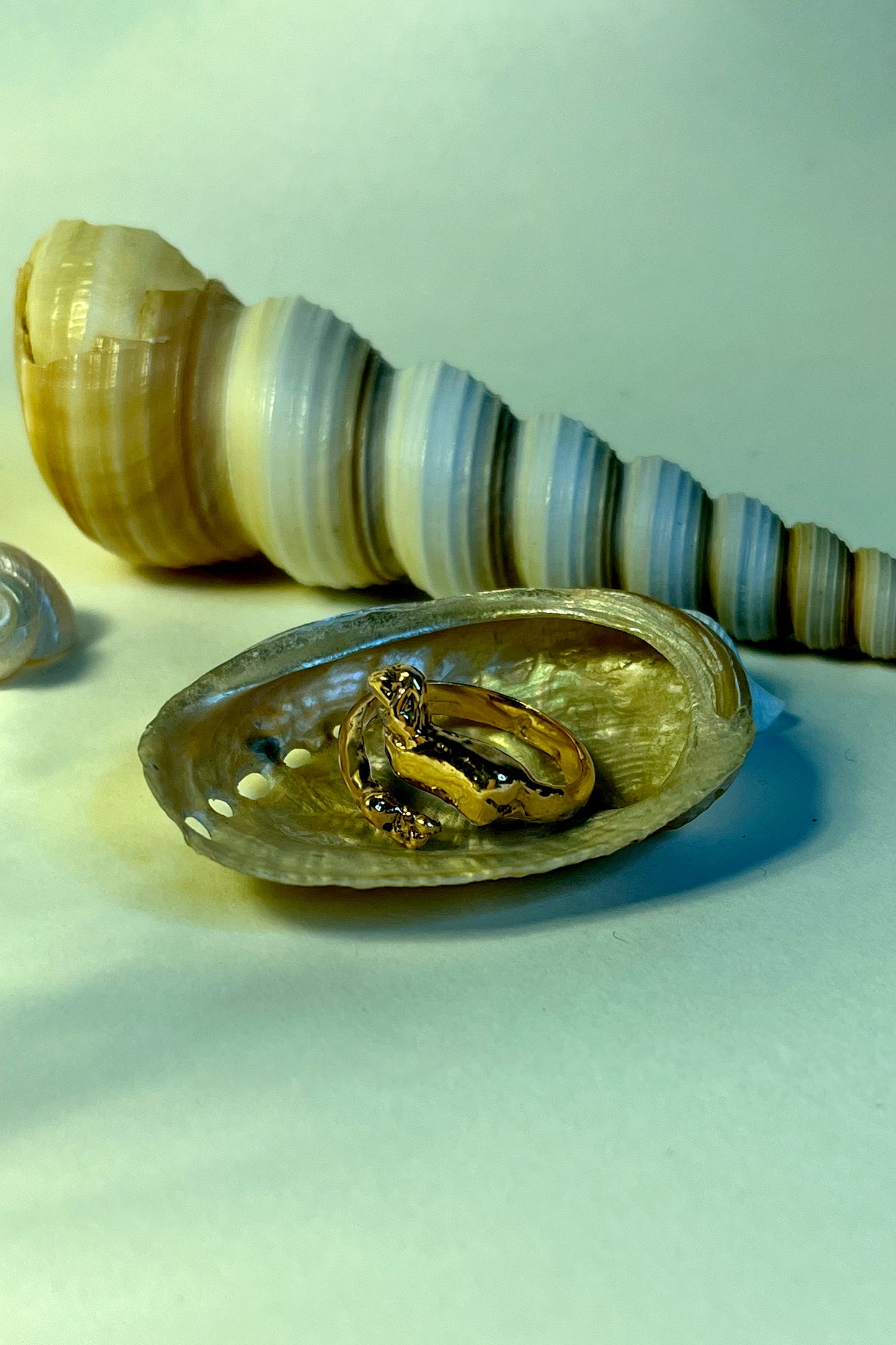 18K Gold Vermeil Cupid ring by CLARK resting inside a shell bathed in an blue underwater light. Hand craft body of a cupid with wings and feet is seen. This is a unique one-of-a-kind item.