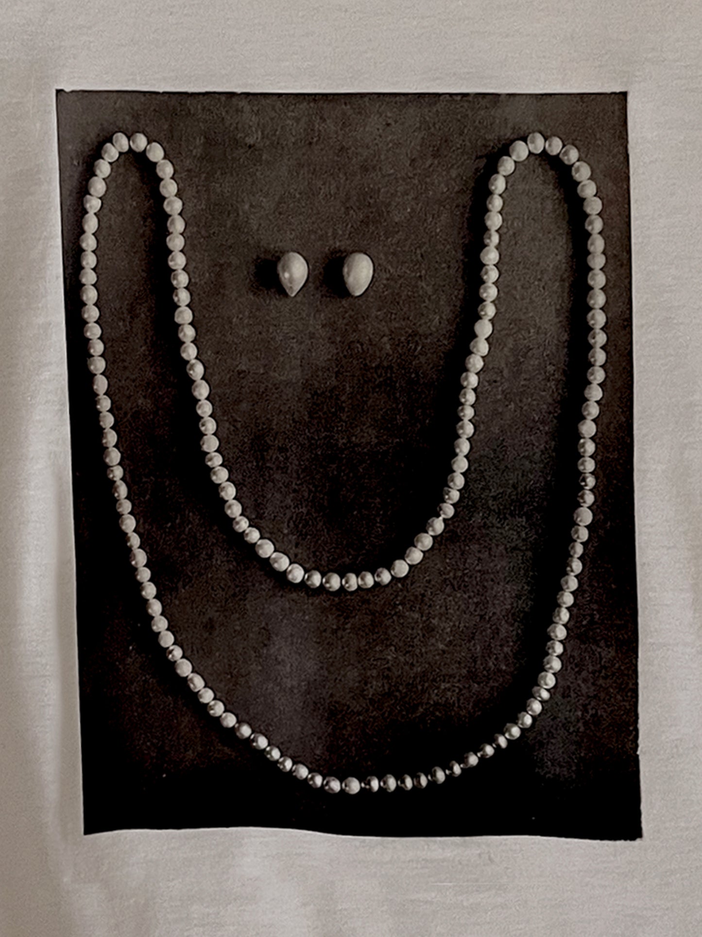 Close up of whimsical design - a pearl necklace and two pearls laid on black pavement in the shape of a smiling face.