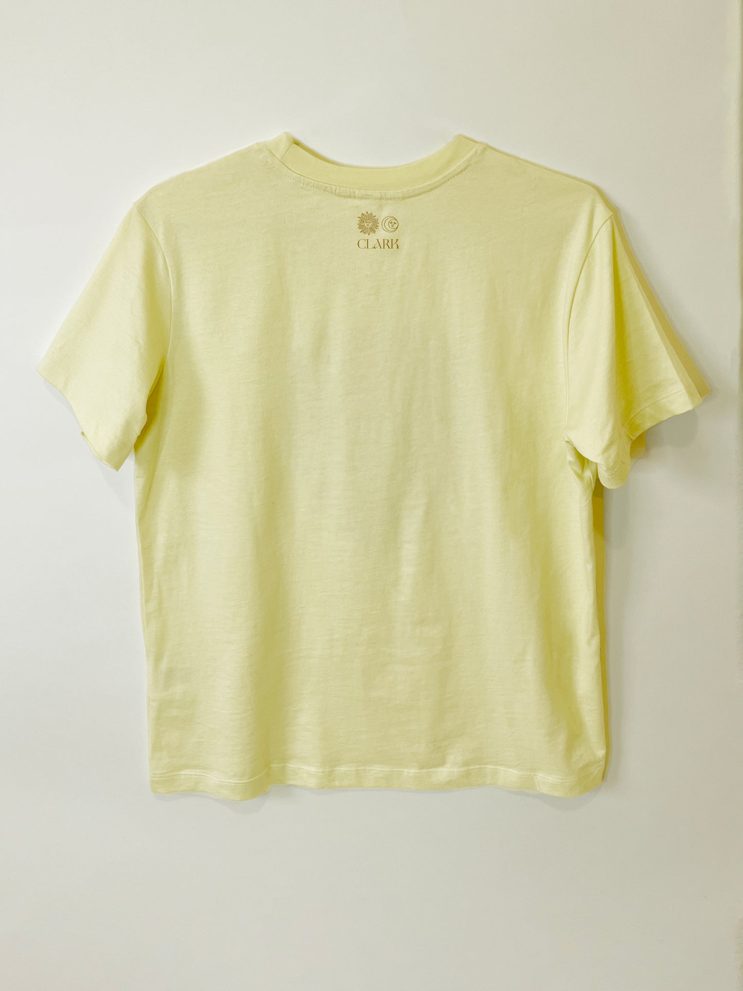 Product photo of Heartbreaker tee by CLARK. The back view of straight-cut black tee with CLARK logo printed in gold at the neck. Logo is of Sun and Moon with CLARK underneath.