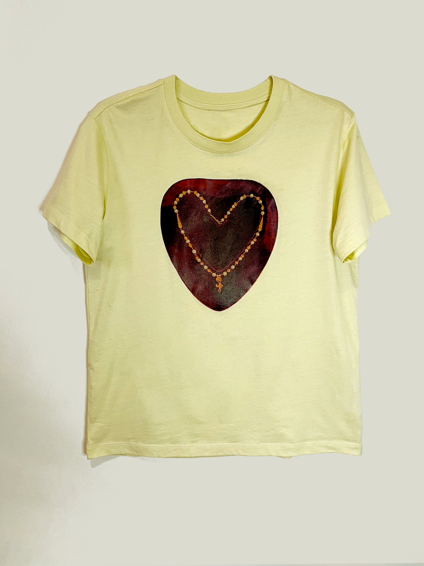 Heartbreaker Tee by CLARK! A yellow graphic tee featuring a photo-collage of a necklace with a baby cupid charm in the shape of a heart on painterly crimson ground, this tee is straight-cut.
