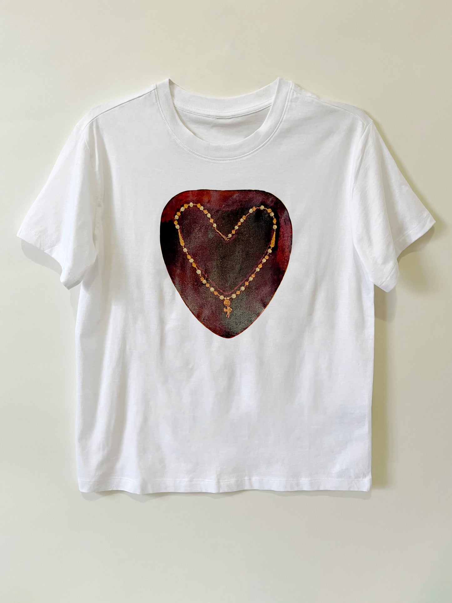 Heartbreaker Tee by CLARK! A white graphic tee featuring a photo-collage of a necklace with a baby cupid charm in the shape of a heart on painterly crimson ground, this tee is straight-cut.