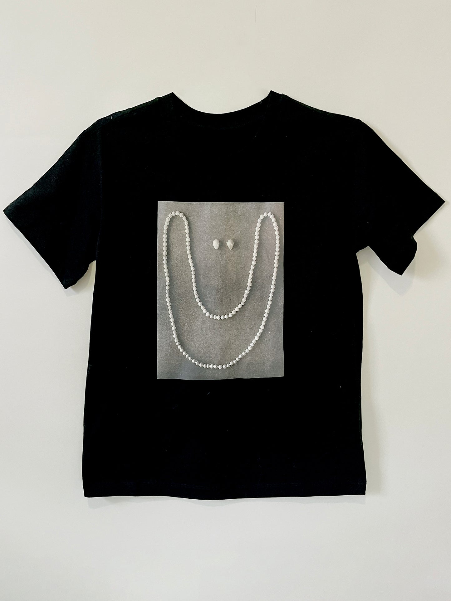 Product photo of Happy As A Clam tee by CLARK. A graphic custom-made black straight-cut shirt featuring a smile made out of pearls. It is an artist made to order item, available in s/m and l/xl.