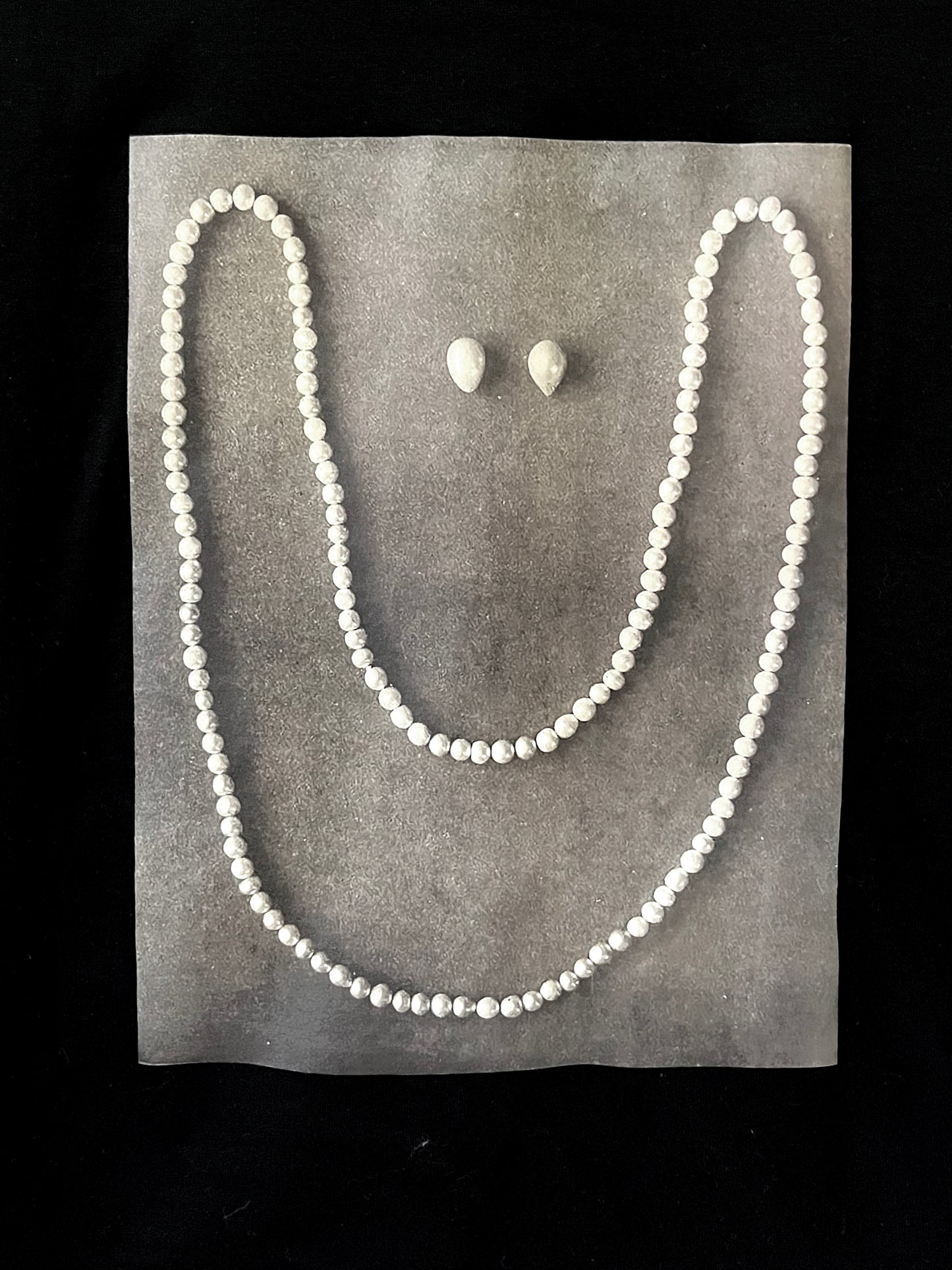 Close up of whimsical design - a pearl necklace and two pearls laid on gray pavement in the shape of a smiling face.