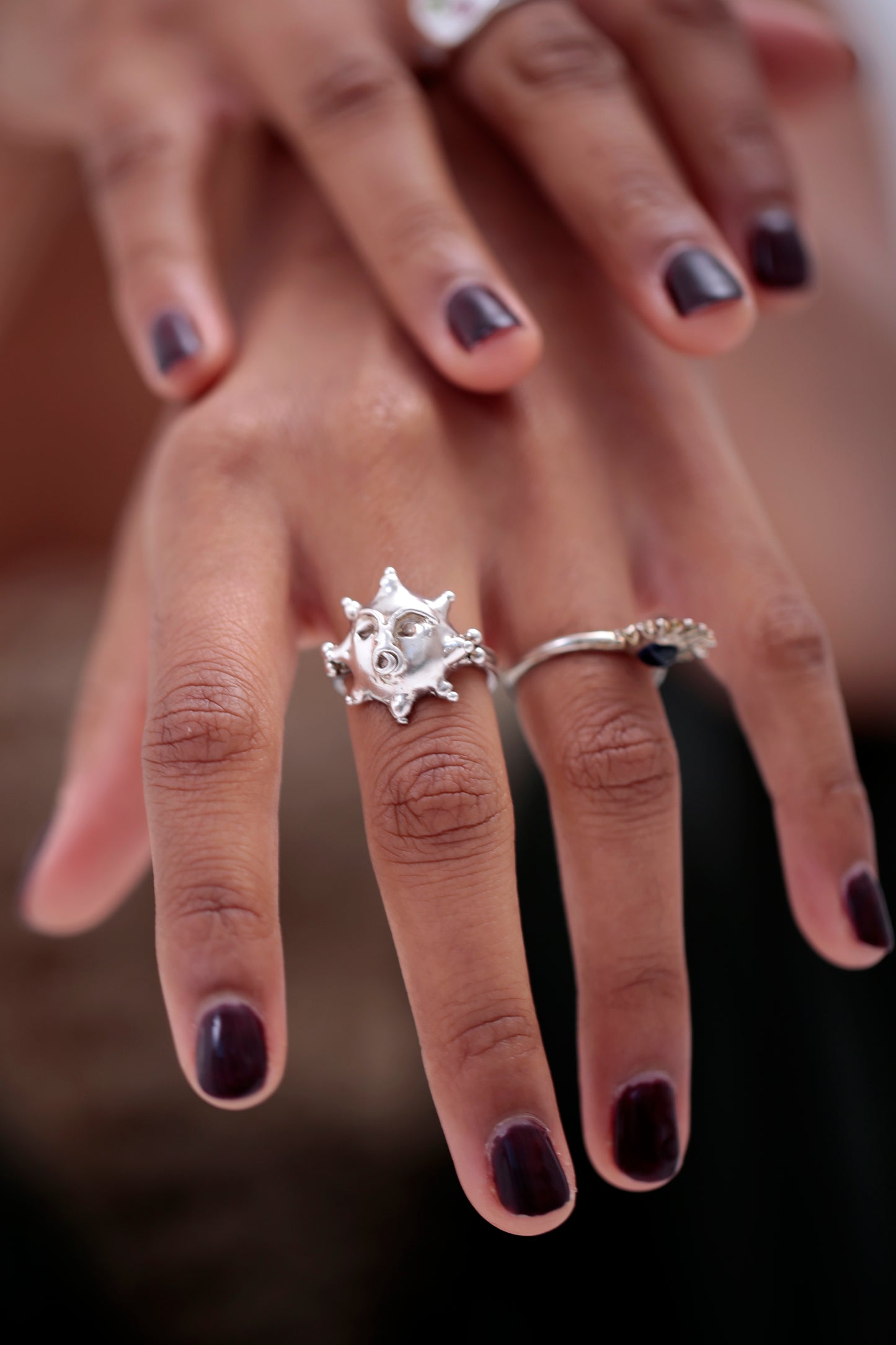 Tempest Ring by CLARK on model’s middle finger. The personified face with a spiral mouth is clearly seen. The Sol ring by CLARK is worn on the ring finger. Both rings are Sterling Silver.