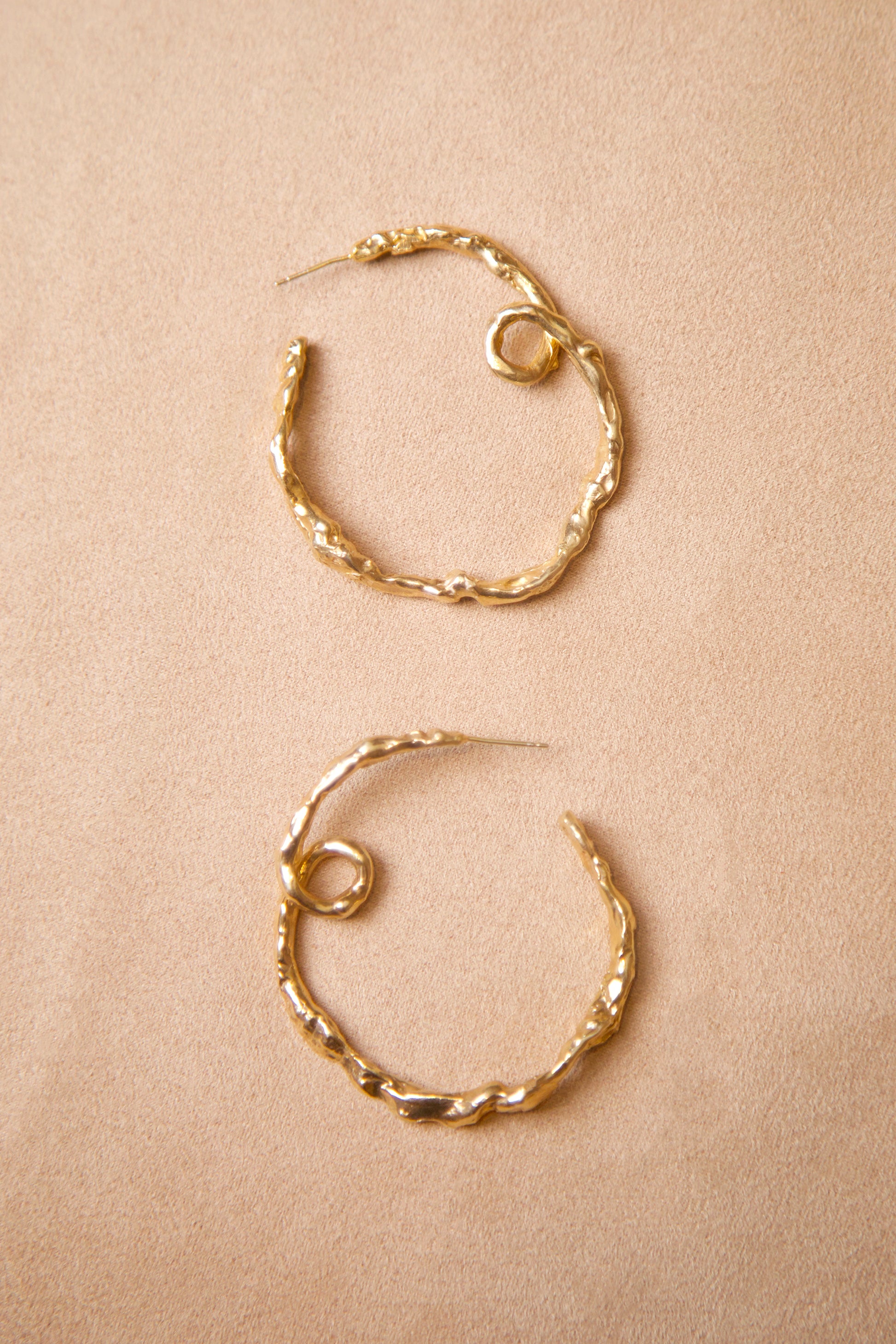 18K Gold Vermeil CLARK Medusa Curl Hoop earrings delicately laid side by side on suede. The unique design is hand made using the lost wax casting method. These sculptural hoops reference a ringlet of hair from the Greek Medusa myth. 