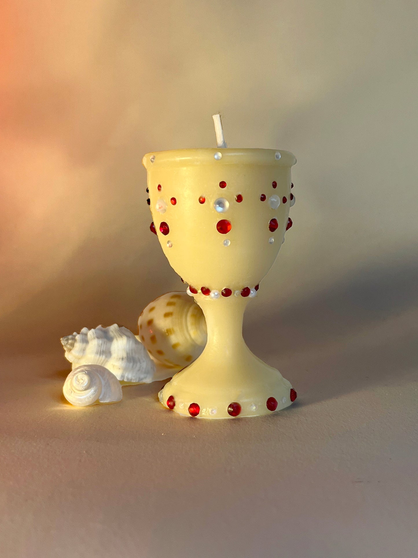 An adorned drinking vessel, shaped like a Victorian wine glass with red and iridescent gemstones. Hand-poured and made from 100% beeswax. Small-batch and a perfect gift for someone looking for an artisanal candle that is eco-friendly and non-toxic.