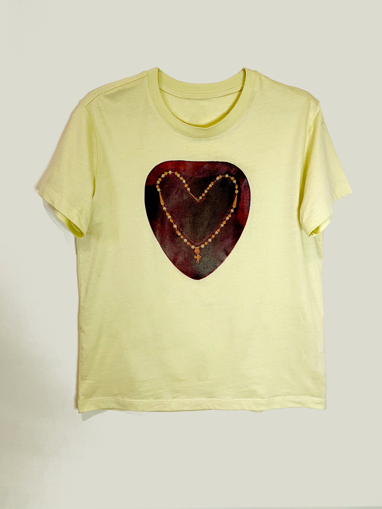 Heartbreaker Tee by CLARK! A yellow graphic tee featuring a photo-collage of a necklace with a baby cupid charm in the shape of a heart on painterly crimson ground, this  tee is straight-cut. 