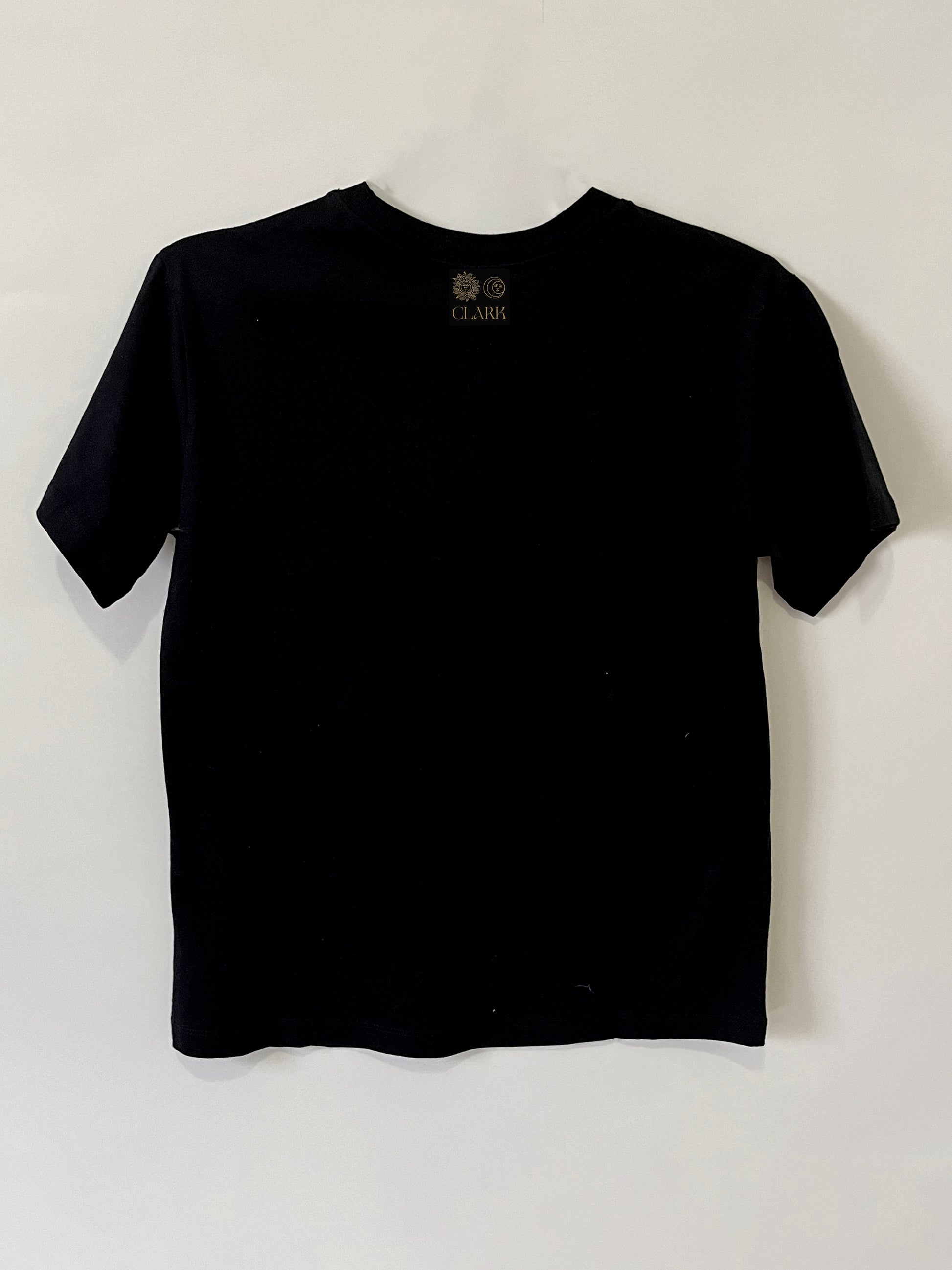Product photo of Happy As A Clam tee by CLARK. The Back view of straight-cut black tee with CLARK logo printed in gold at neck. Logo is of Sun and Moon with CLARK underneath. 