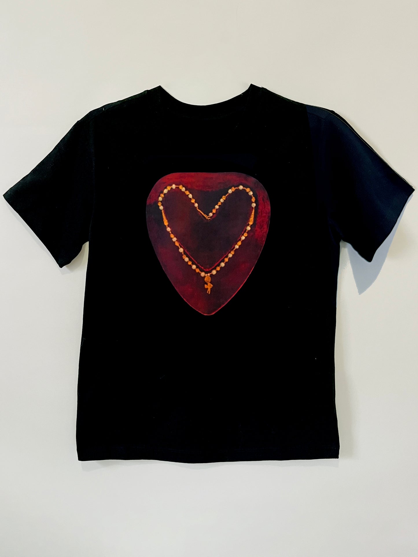 Heartbreaker Tee by CLARK! A black graphic tee featuring a photo-collage of a necklace with a baby cupid charm in the shape of a heart on painterly crimson ground, this  tee is straight-cut. 