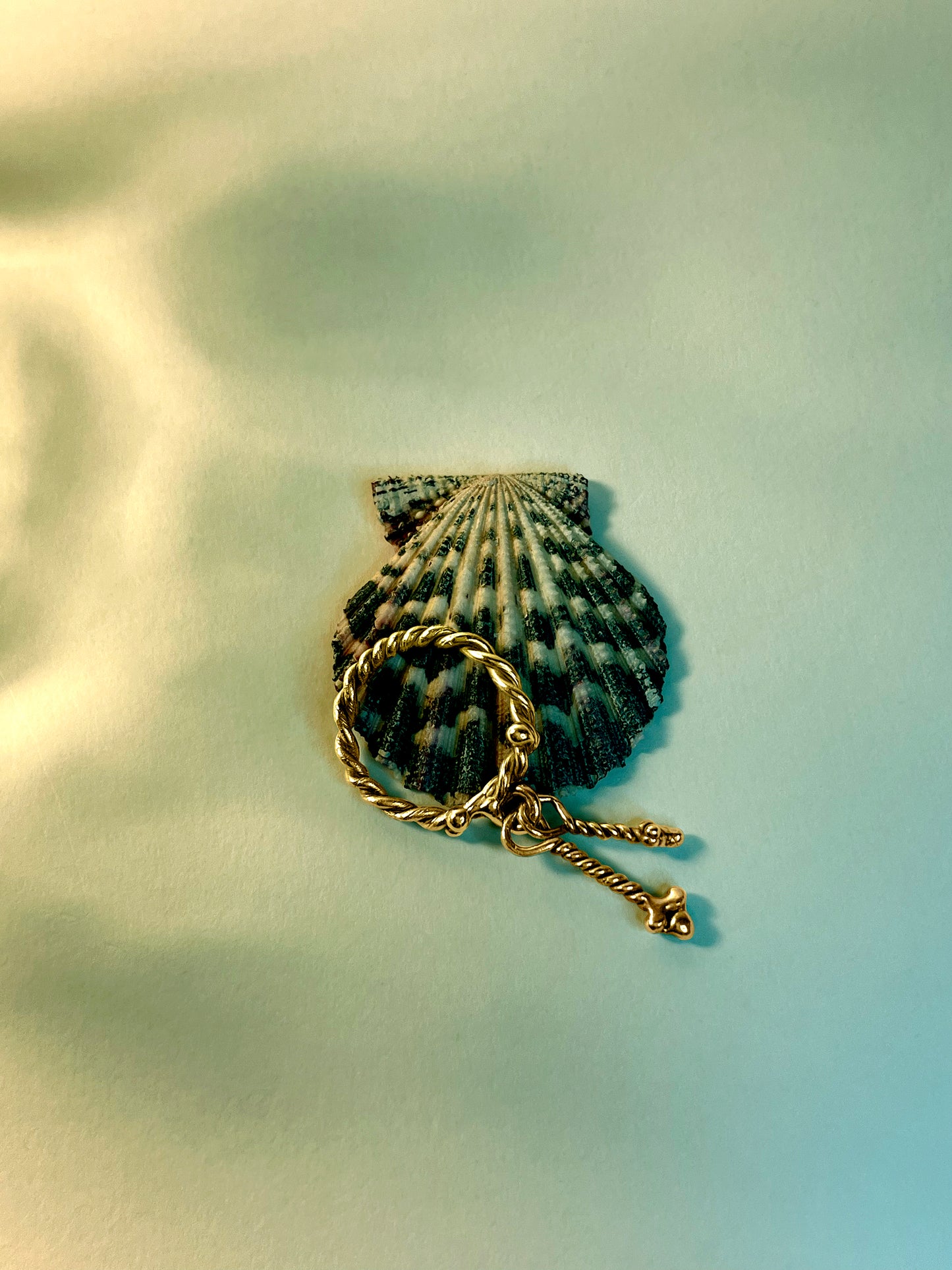 A 18K Gold Vermeil Twisted Fates Ring by CLARK rests against a seashell. Bathed in a dappled blue light - the scene feels organic and mystical. This ring is hand-made using the lost wax cast method so each charm is unique and one-of-a-kind. 
