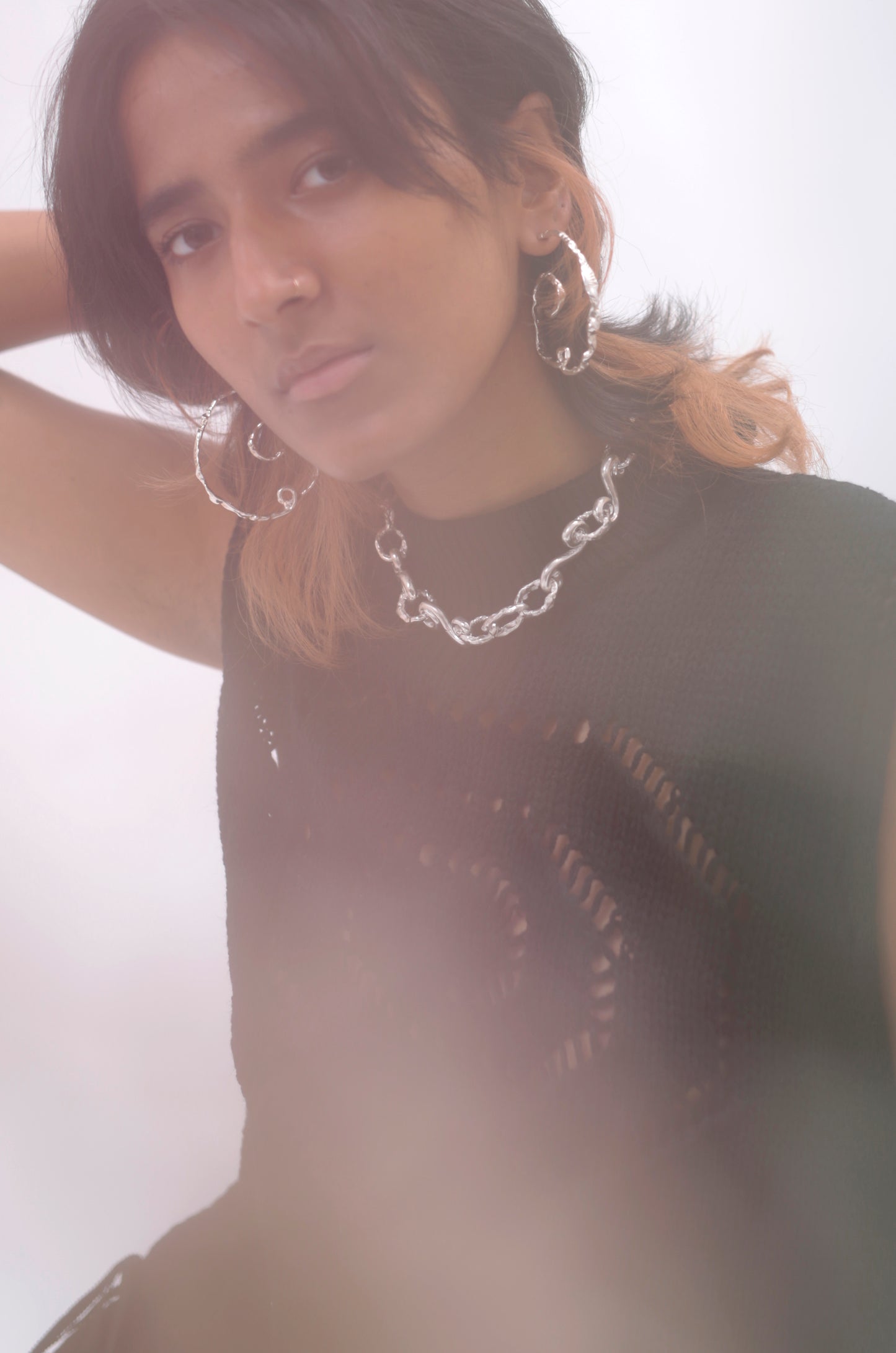 ¾ View of model with hazy filter. Model is looking into the camera and wearing CLARK Andromeda Earrings and CLARK Braided Waves Necklace. These pieces are Sterling Silver and a classic and elevated complement to one another. 