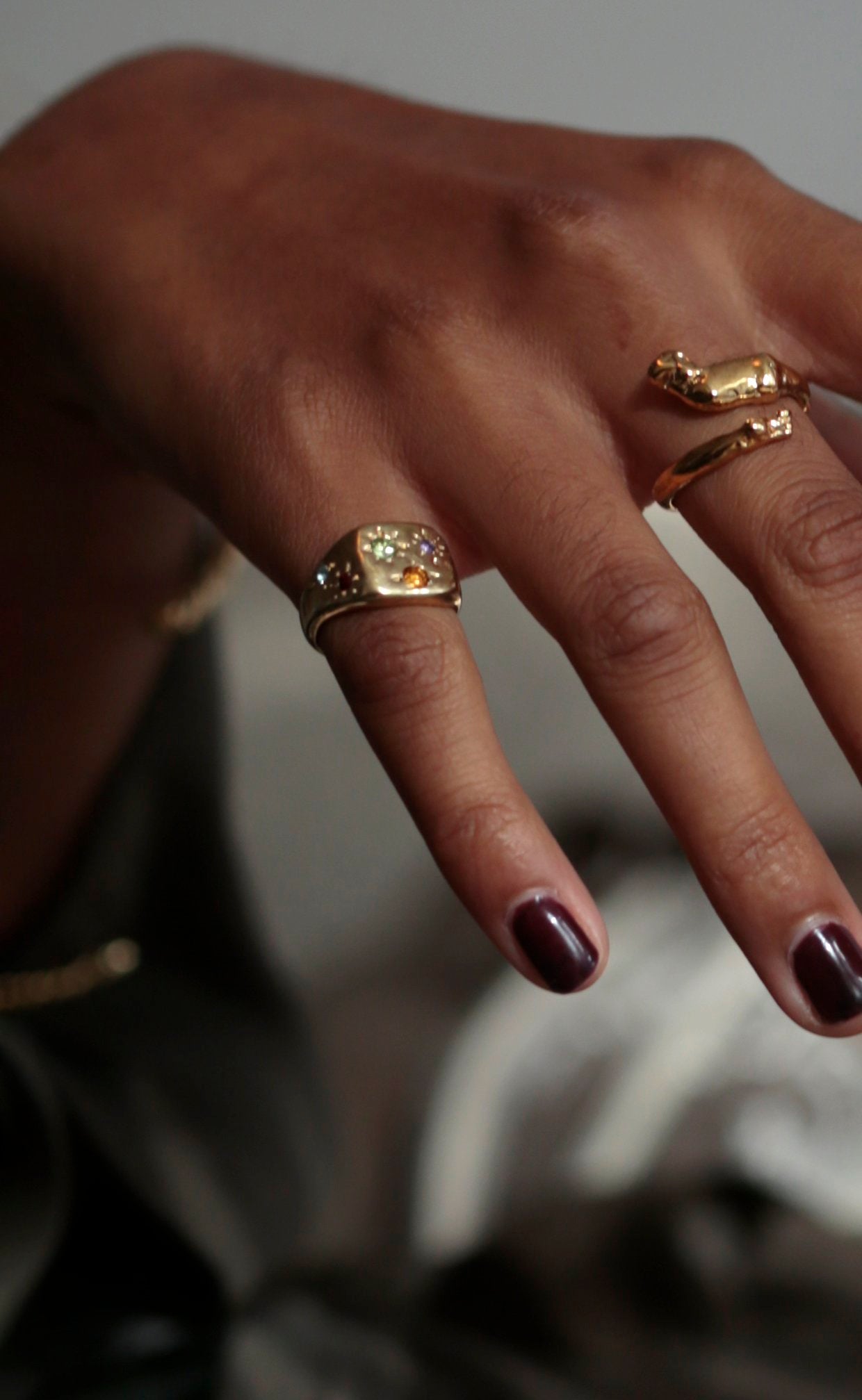 Detail photo of CLARK Constellation Signet ring in 18K Gold Vermeil. The ring is flush-set with multi-colored gems on the model's  pinkie finger. The hand and model are relaxed. The jewelry feels elevated, luxurious and one-of-a-kind.