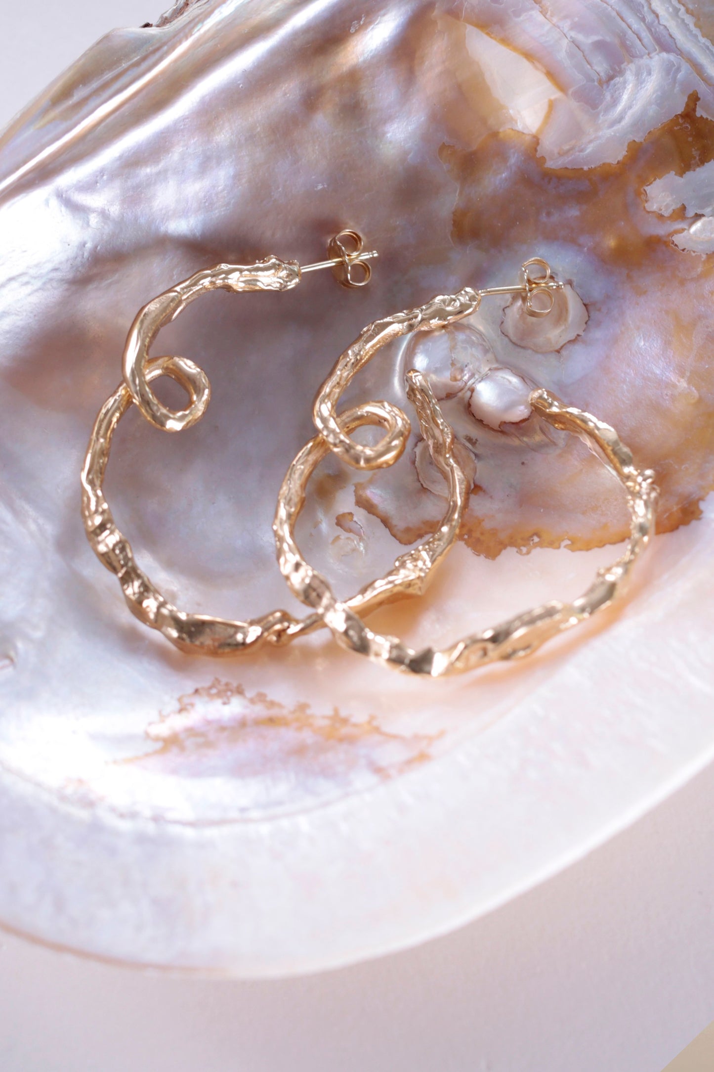 18K Gold Vermeil CLARK Medusa Curl Hoop earrings delicately laid side by side in an iridescent shell. The unique design is hand made using the lost wax casting method. 