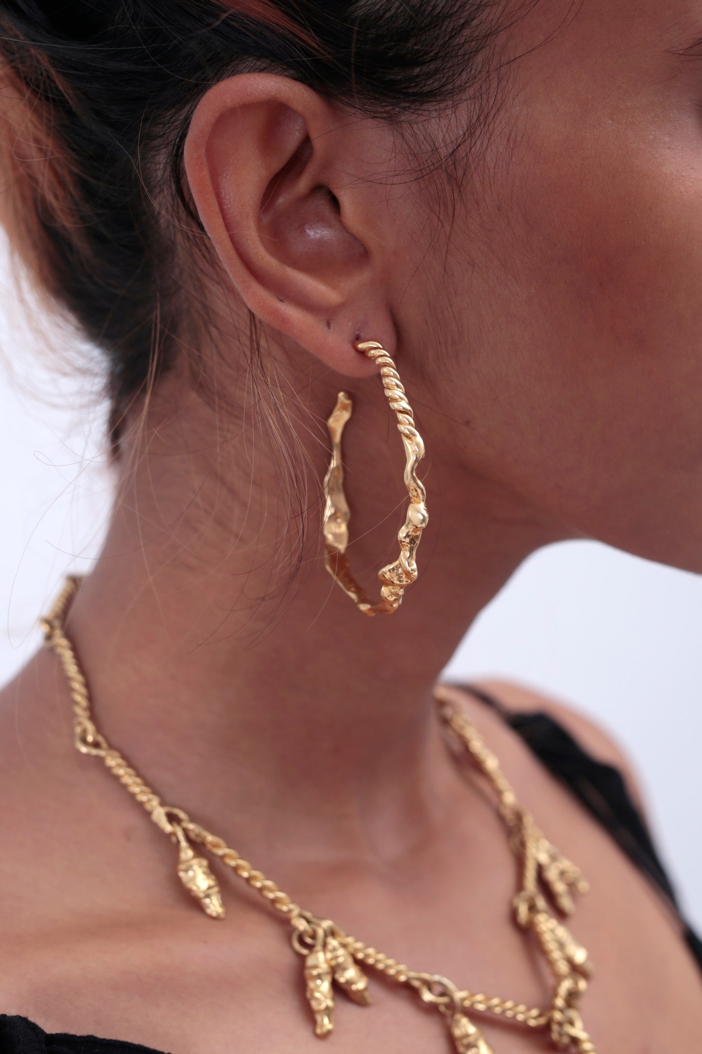 Side view of model wearing CLARK Sea Siren Hoops. This is a unique midsize 18K Gold Vermeil hoop. The photo shows handmade details of seashells and nods to the mermaid's tail. Model also is wearing a Heavenly Bodies Necklace, a special occasion essential. 