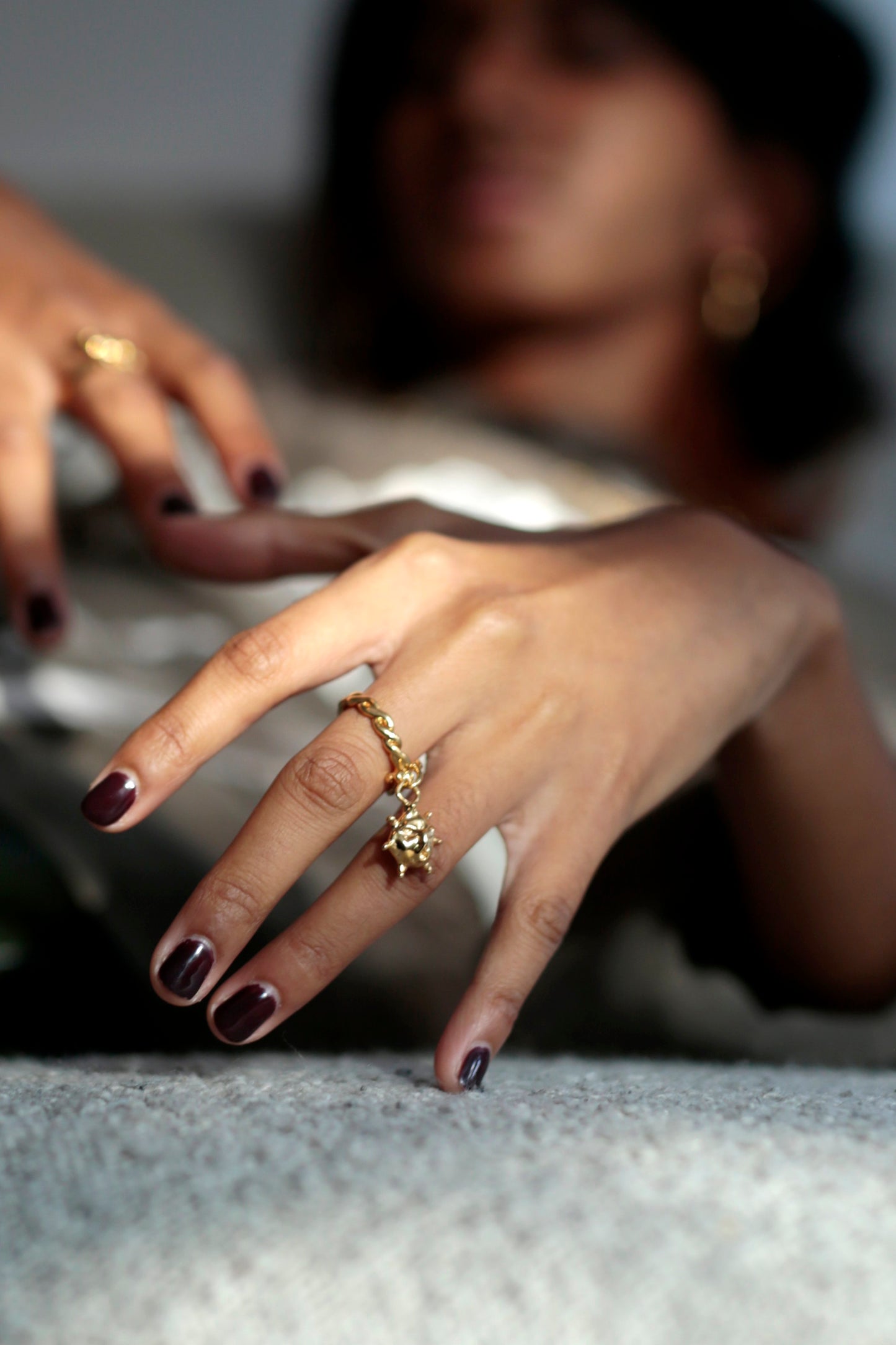 CLARK detail shot. A hand bathed in sunlight is seen in the foreground, a CLARK 18K Gold Vermeil Aurora Charm ring is on the middle finger. This ring is hand craft and made to order. 