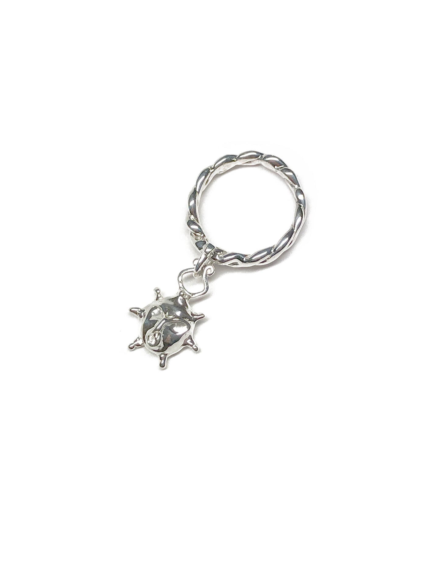 Product photo of the CLARK Aurora Charm Ring in Sterling Silver. Shot on white ground, this unique statement ring has a dangle charm. It has a twisted band with a loop on the top, attached is a silver sun talisman. Its mouth is a spiral and it has six points, like sun rays. This classic ring is made using the lost wax casting method. It is hand craft and made to order.