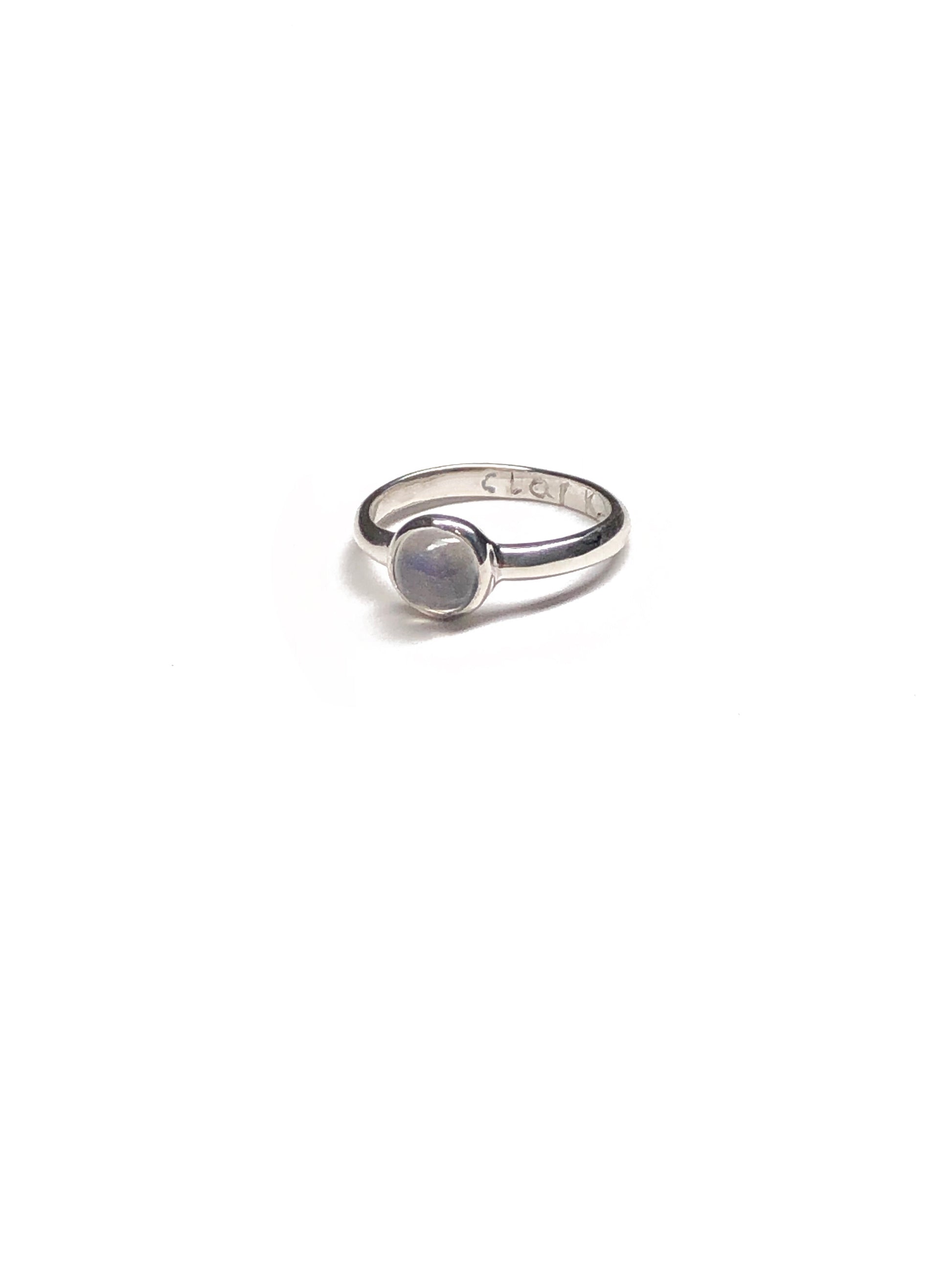 Product photo of Magic Moonstone Ring by CLARK shot on white. Ring shows cabochon set moonstone and hand engraved “CLARK.” The ring is sterling silver and made using the lost wax casting method. 